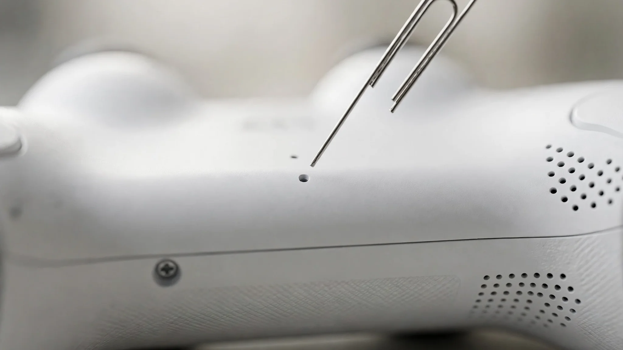 paperclip pressing the reset pinhole on the back of a DualSense controller